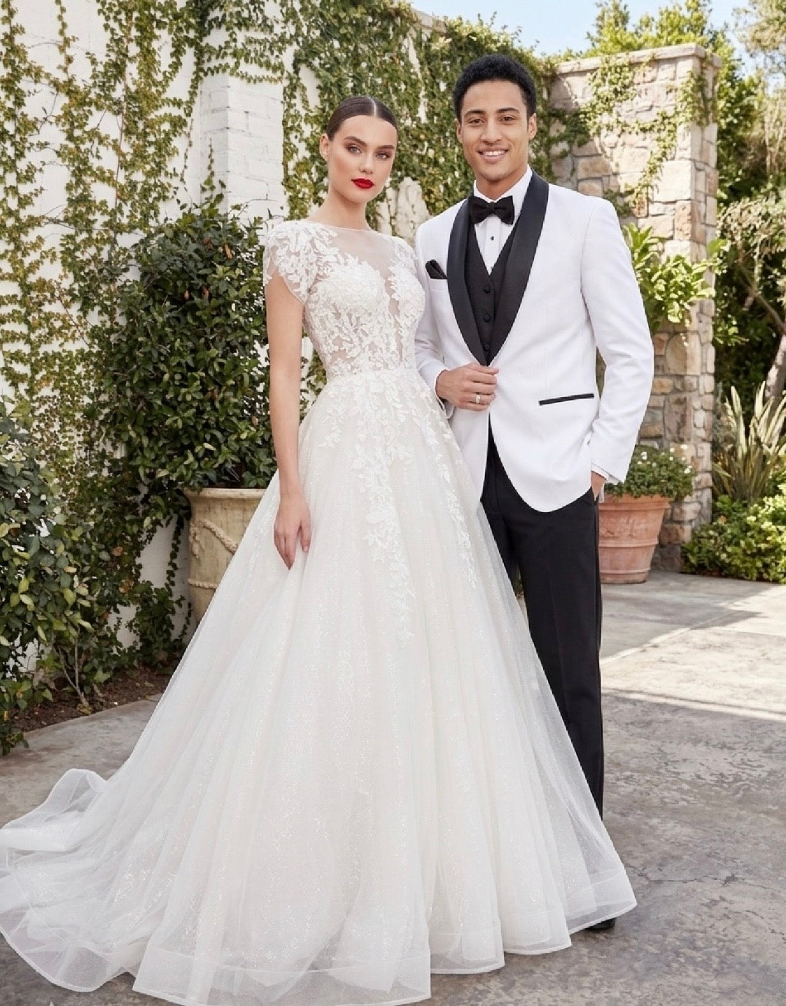 Man in a tuxedo and woman in a white wedding dress standing together outdoors.