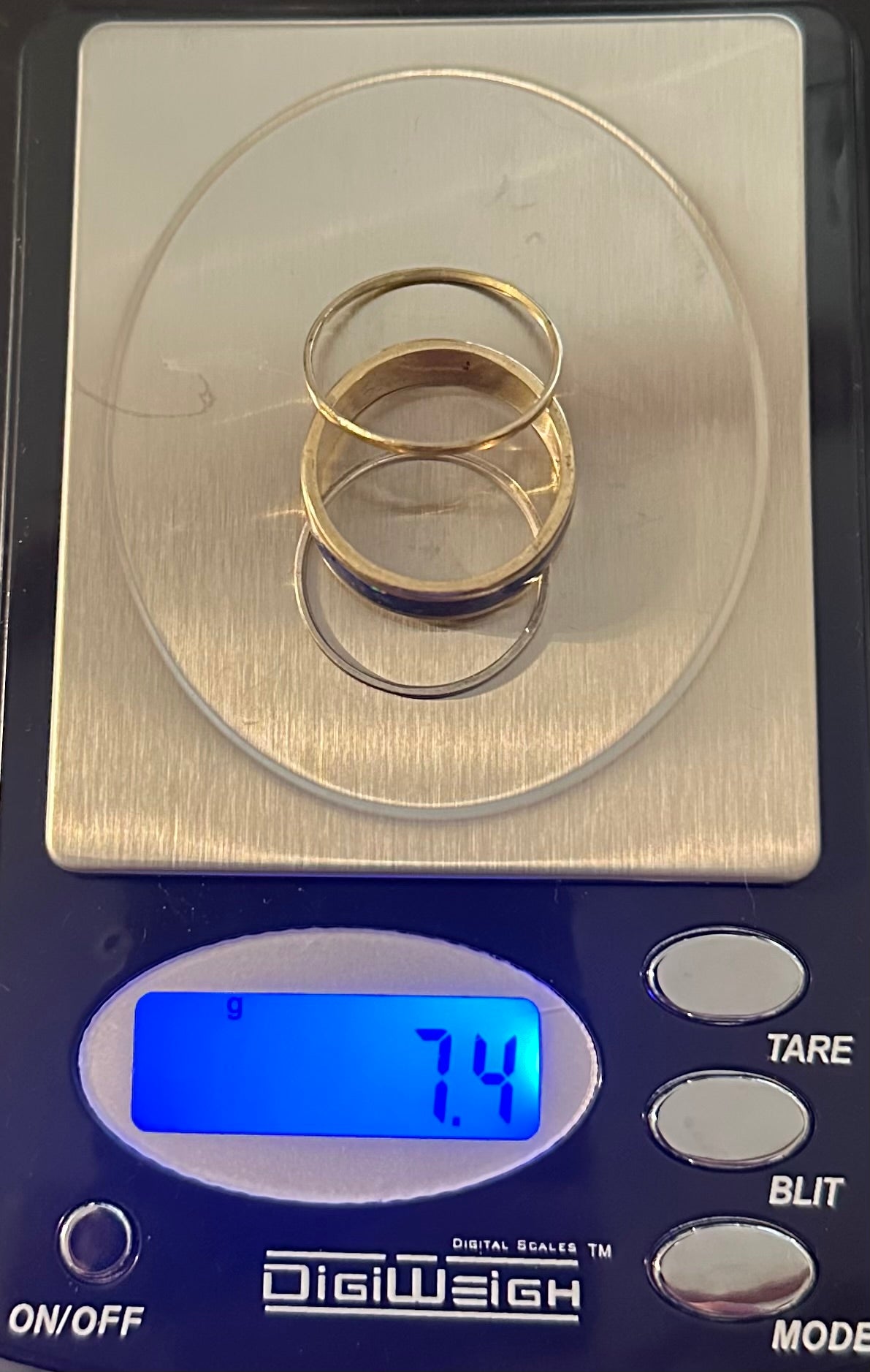Digital scale showing 7.4 grams total weight for the Masterwork Artisan Trio gold and silver ring set.