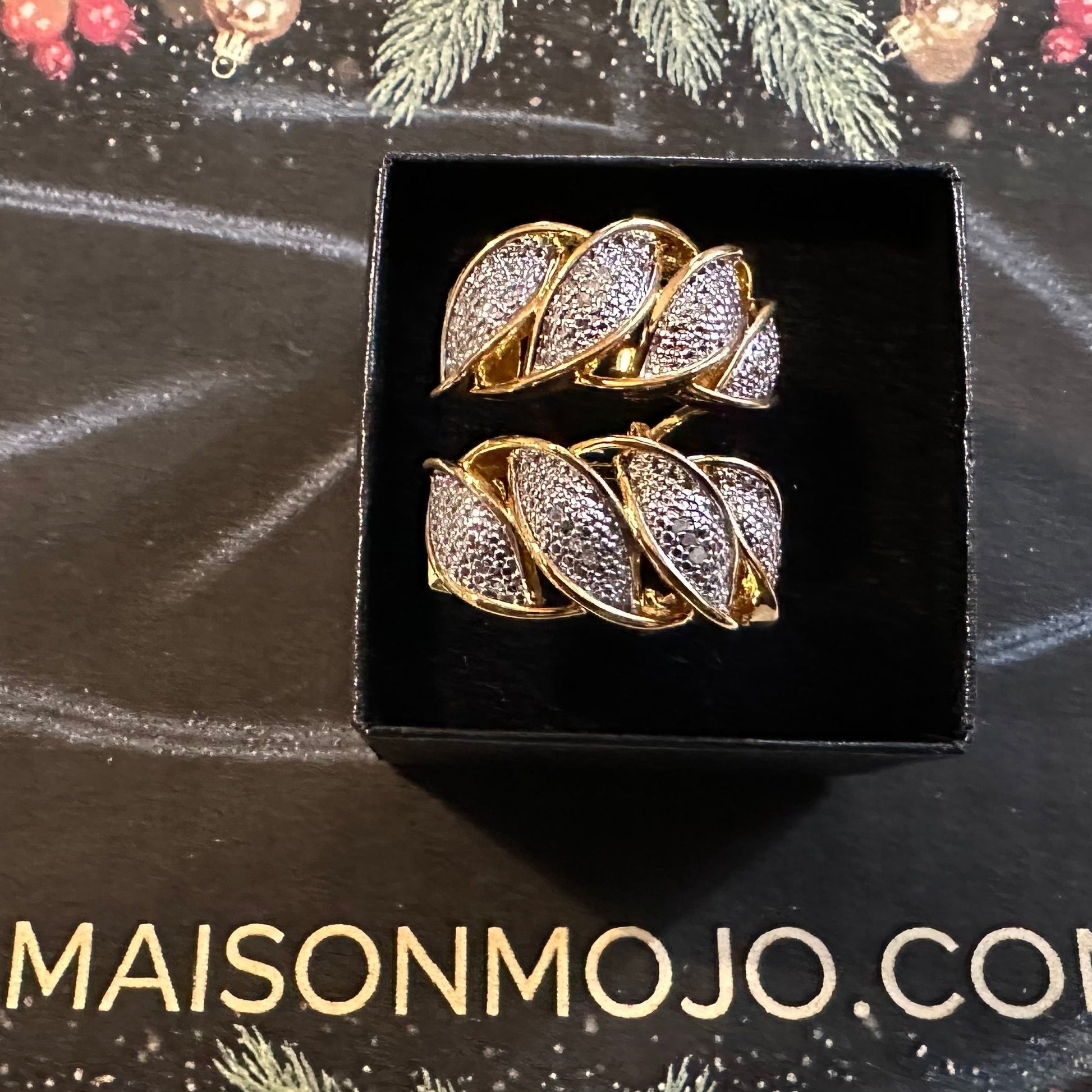 Pair of gold and diamond earrings in a black box on a dark background with 'MAISONMOJO.COM' branding.