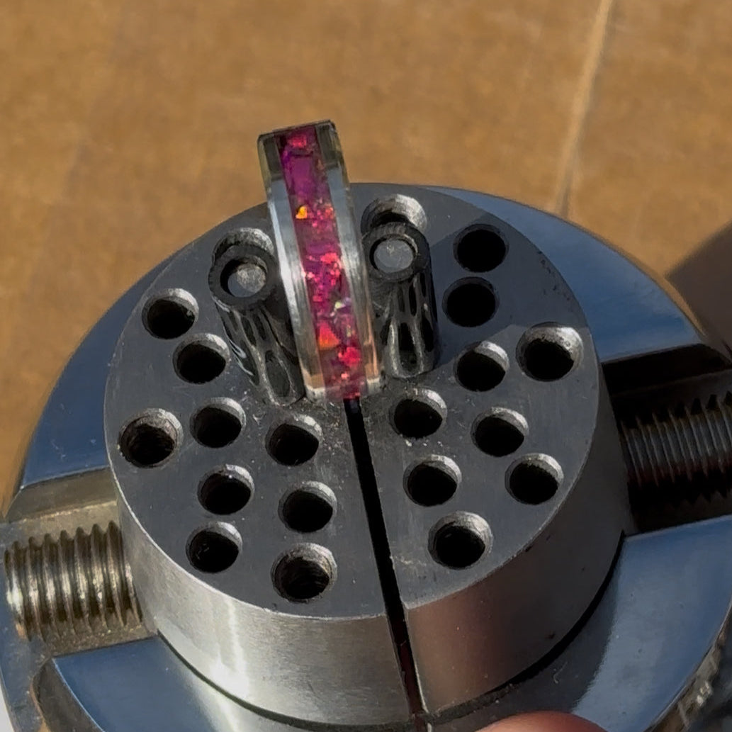 Close-up of a metal ball vice with a pink pink Opal inlay on a wooden surface