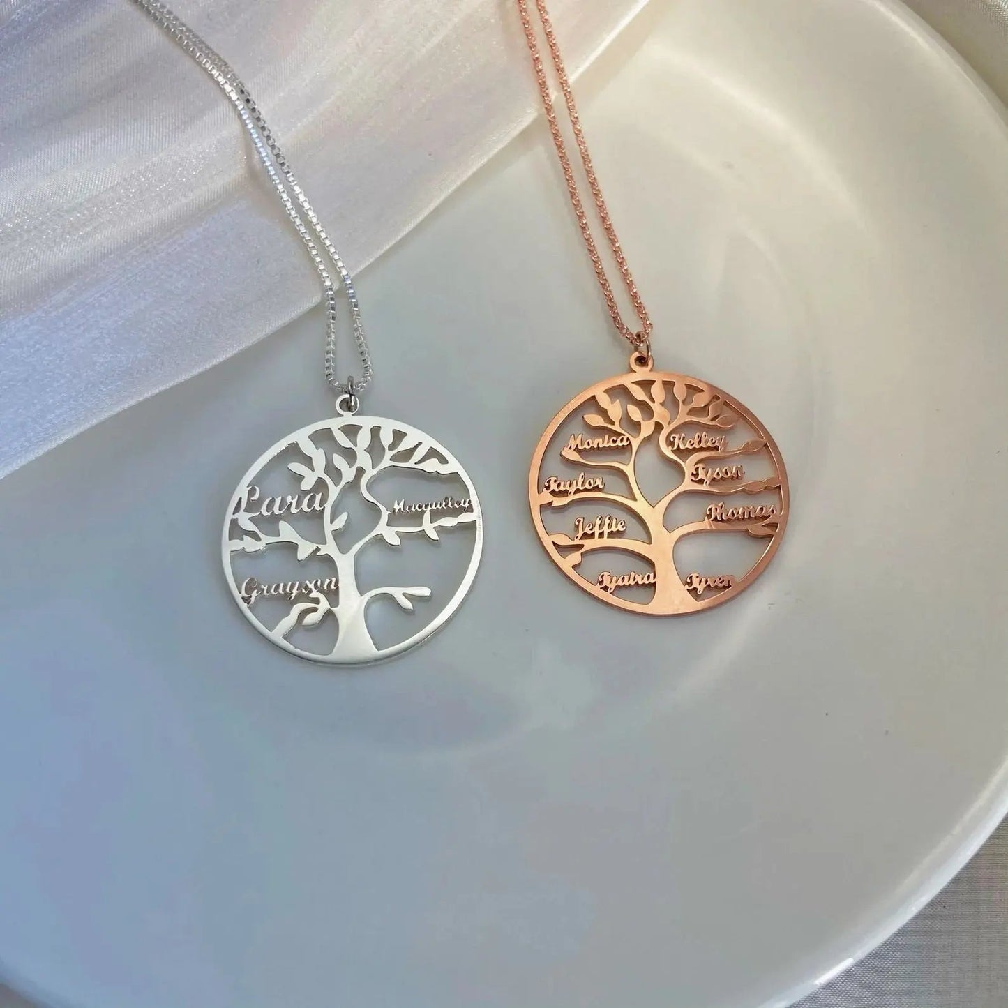Two tree-shaped necklaces, one silver and one gold, on a white plate.