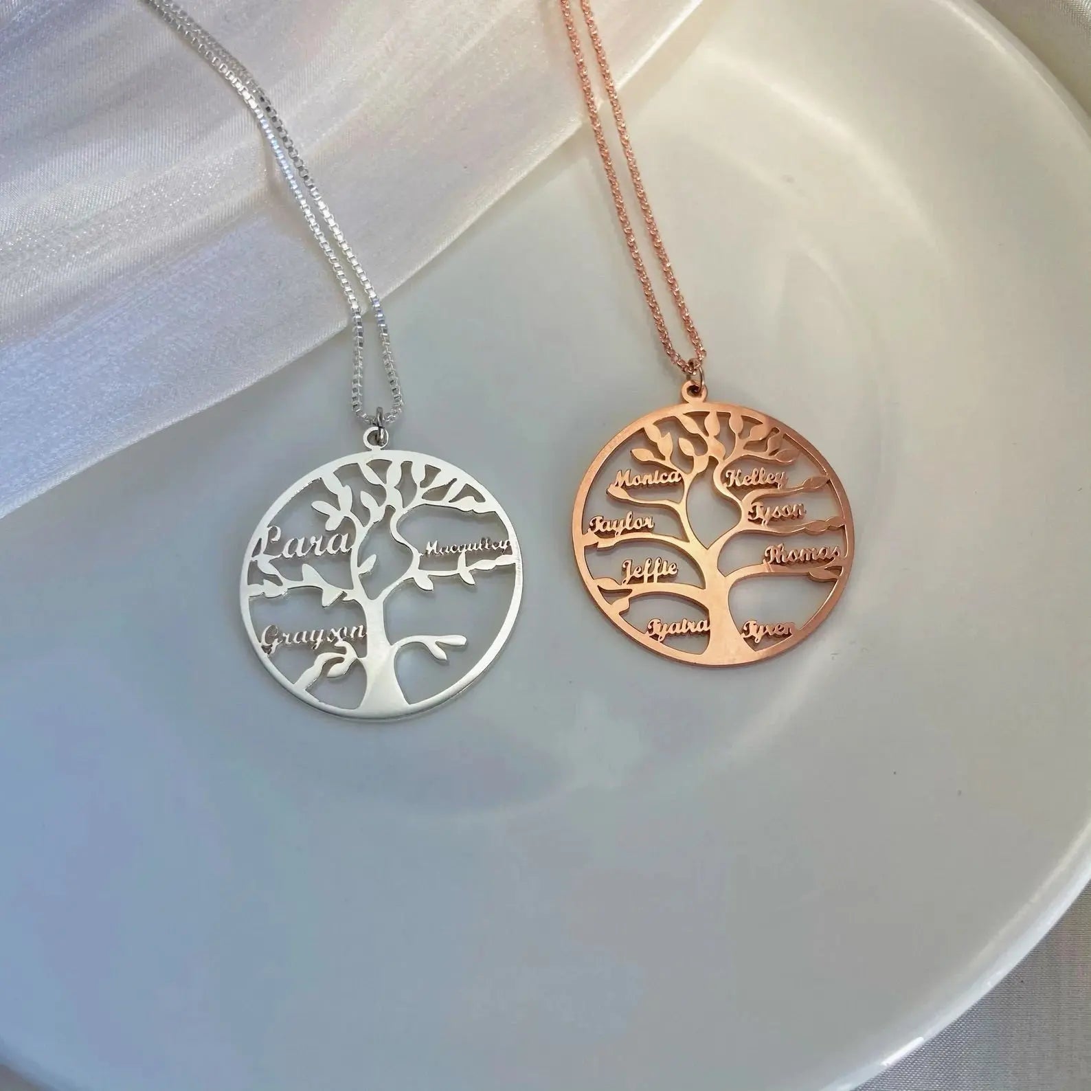 Two tree-shaped necklaces, one silver and one gold, on a white plate.