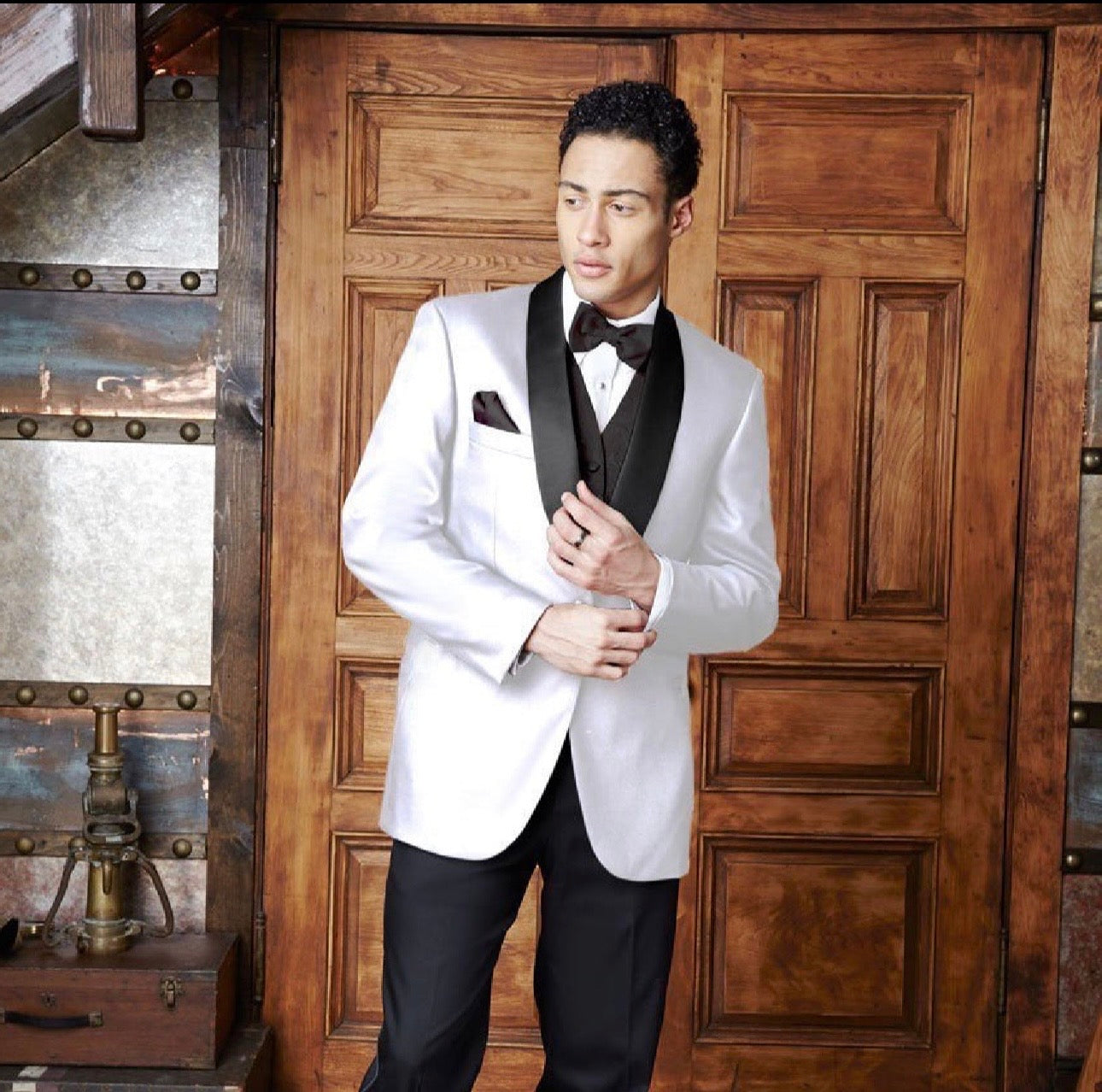 Man in a white tuxedo standing in front of a wooden door.