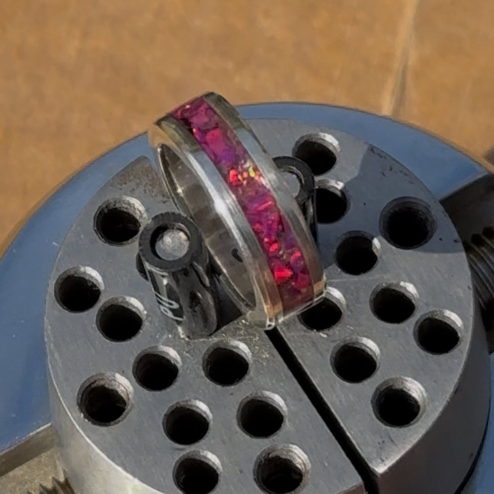 Silver ring with pink gemstone on a metal cylindrical object