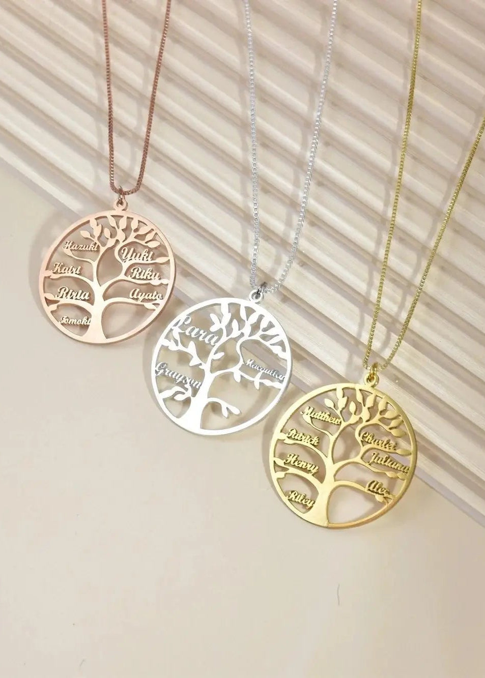 Three tree-shaped necklaces in gold, silver, and rose gold on a neutral background