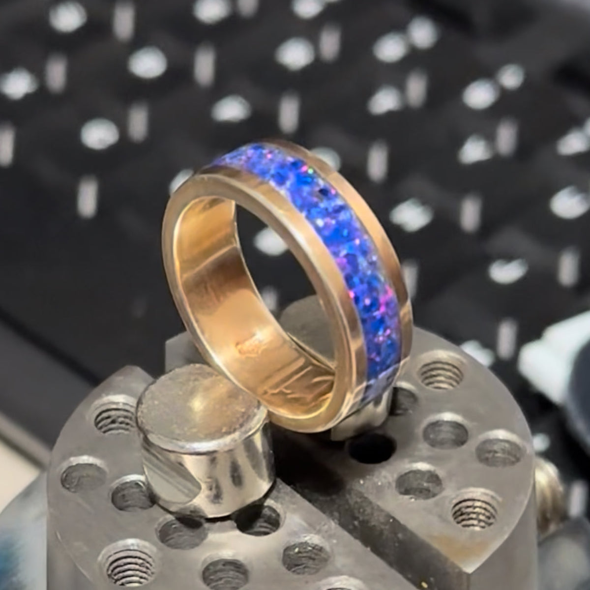 Gold ring with blue and purple opal inlay on a metallic stand with a blurred background