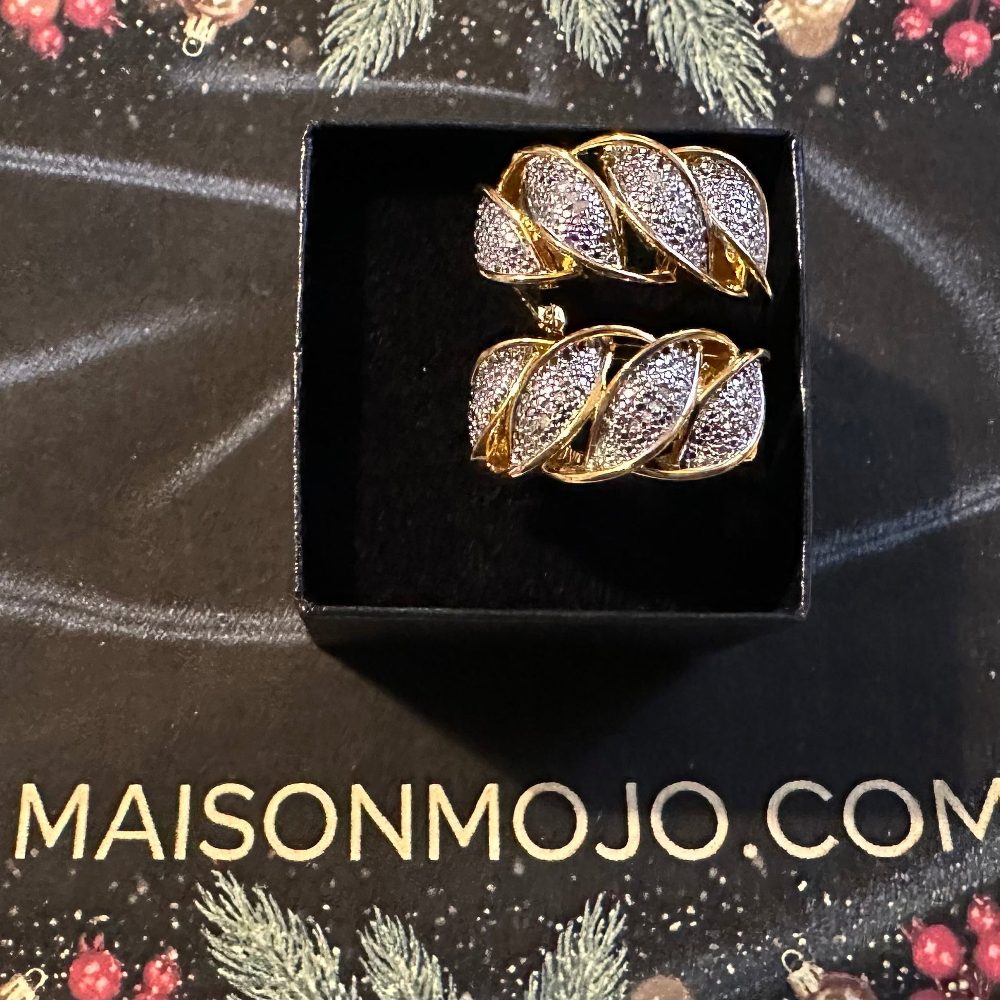 Gold and diamond earrings in a black box on a festive background with 'MAISONMOJO.COM' text.
