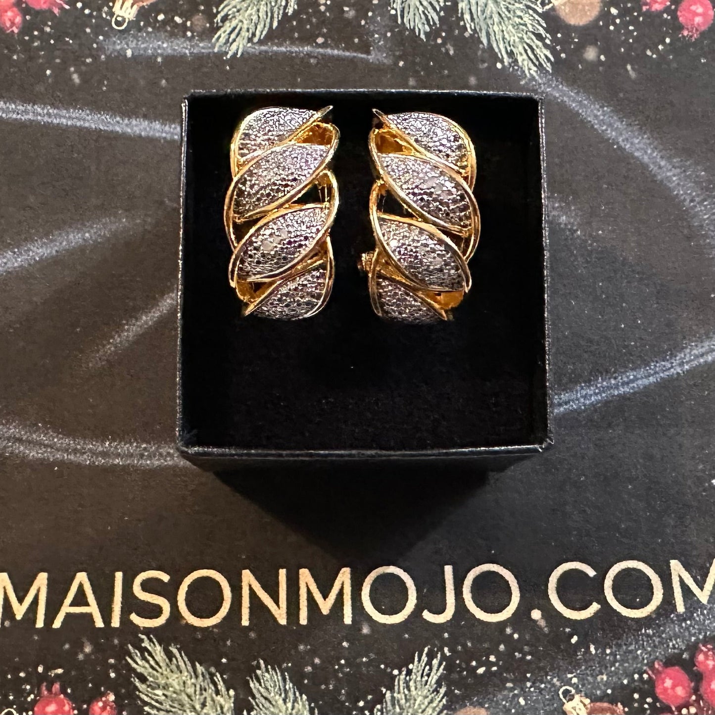 Pair of gold and diamond accent spiral earrings in a black box on a decorative background with 'MAISONMOJO.COM' text.