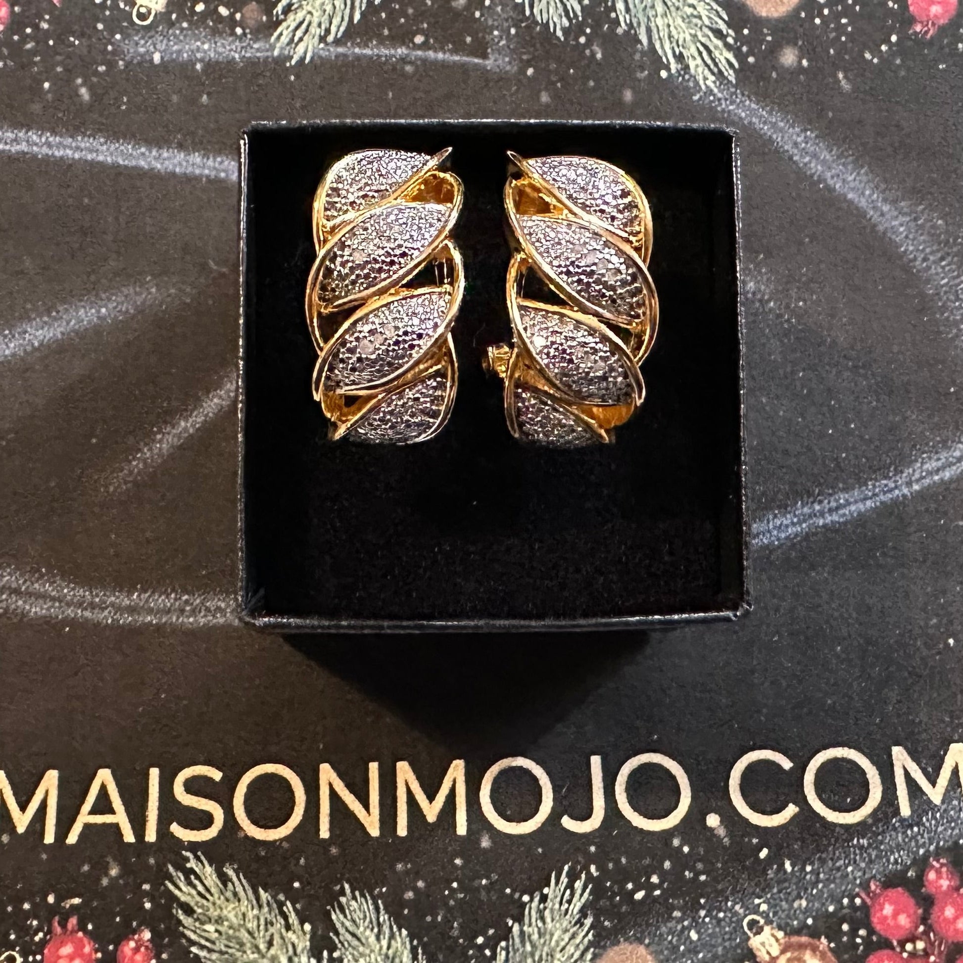 Pair of gold and silver earrings in a black box on a decorative background with 'MAISONMOJO.COM' text.