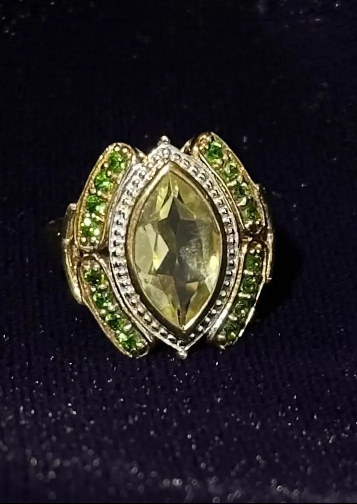 Gold ring with a large yellow gemstone and smaller green stones on a black background
