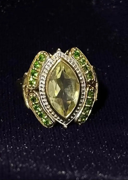 Gold ring with a large yellow gemstone and smaller green stones on a black background