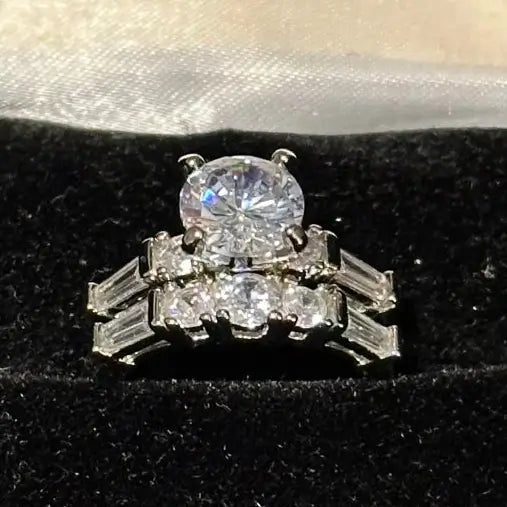 Close-up of a women’s halo engagement ring and matching silver band. The brilliant-cut diamond simulants catch the light, highlighting the intricate rhodium-plated sterling silver craftsmanship.
