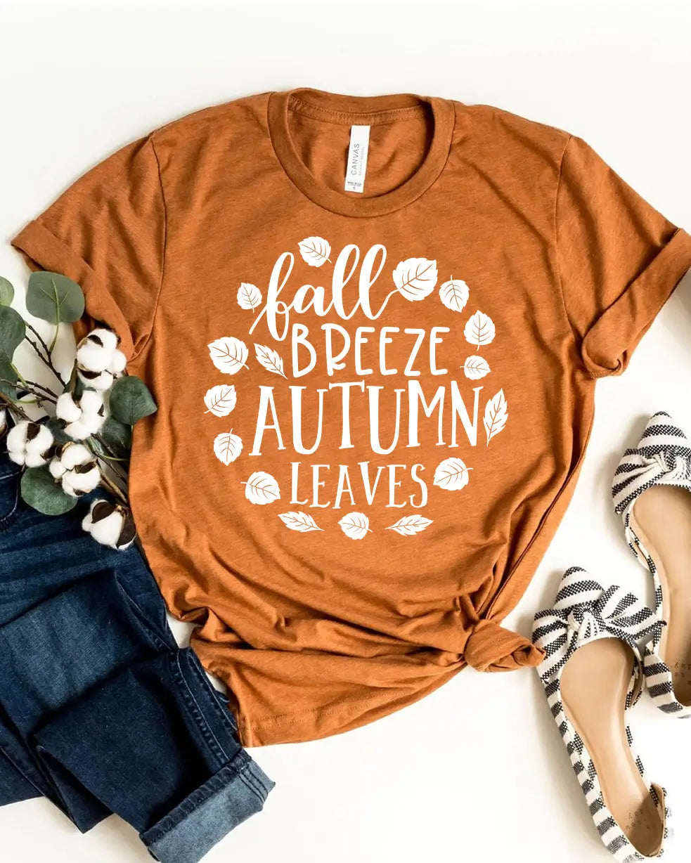 Orange t-shirt with 'fall breeze autumn leaves' text and leaf graphics on a white background.