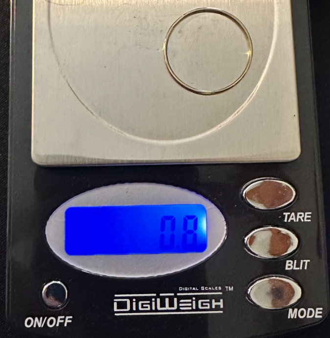 Digital scale with a small gold ring on the platform, displaying '0.8' on the screen.