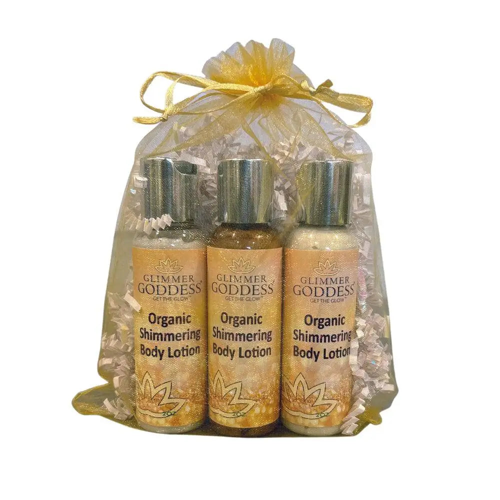 Three bottles of Glimmer Goddess Organic Shimmering Body Lotion in a clear bag with a yellow ribbon on a white background.