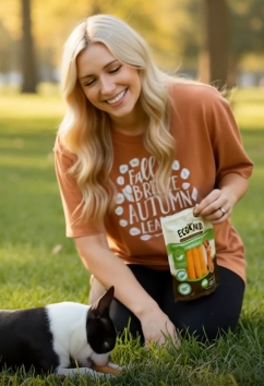 Woman in an orange shirt with a dog, holding a package in a park